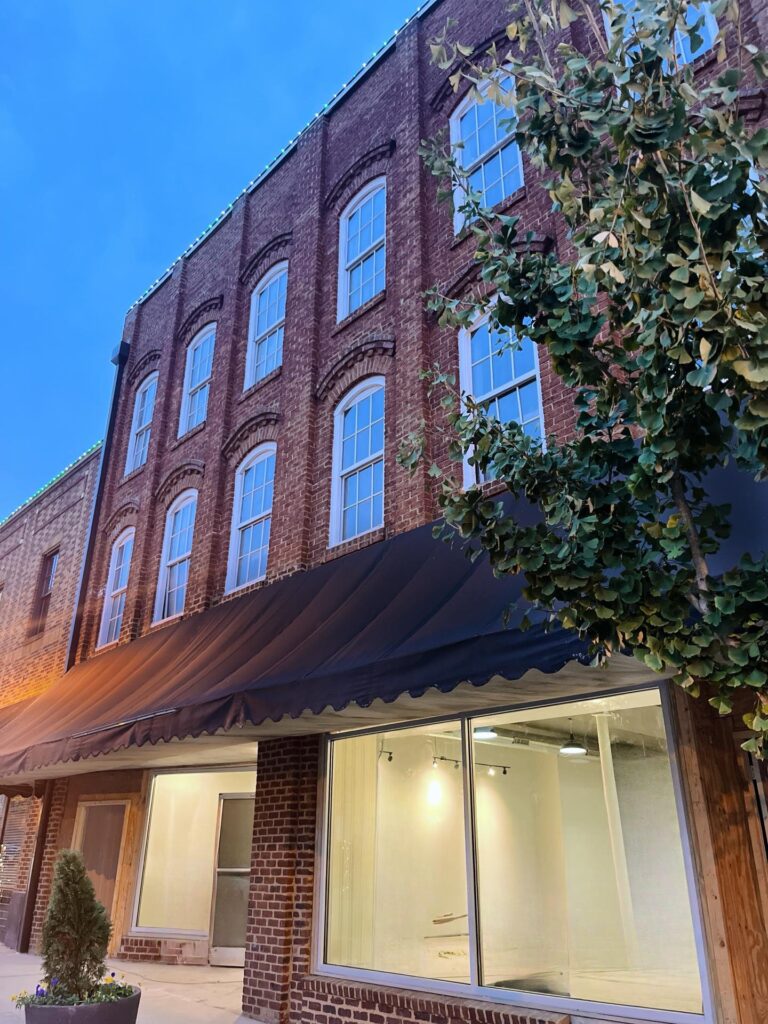 Exterior view of Murphy’s On Main in downtown Monroe, featuring a historic brick building with large display windows, black awning, and upper-story windows lit against the evening sky.